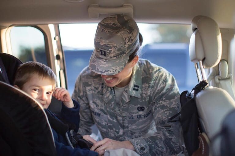 Featured image for Military Auto Insurance, showing a female servicemember securing her child in the car seat of her vehicle